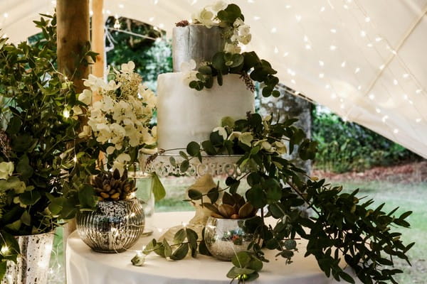 Silver and white wedding cake covered in foliage