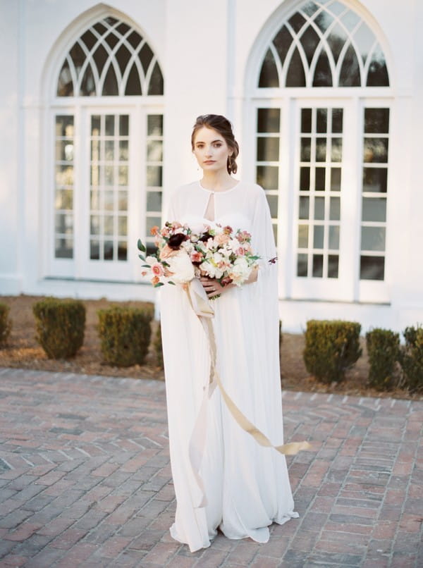 Bride wearing cape holding bouquet