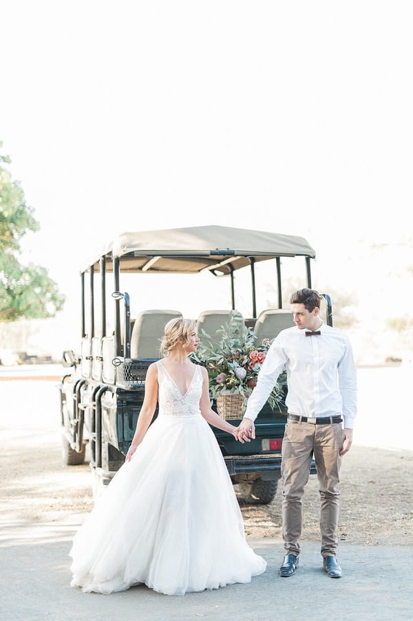 Bride and groom holding hands in front of safari truck