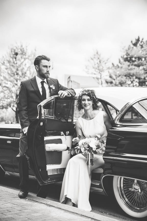 Bride sitting in Cadillac wedding car as groom stands by door