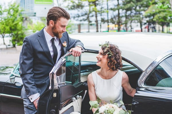 Groom smiling at bride sitting in Cadillac wedding car