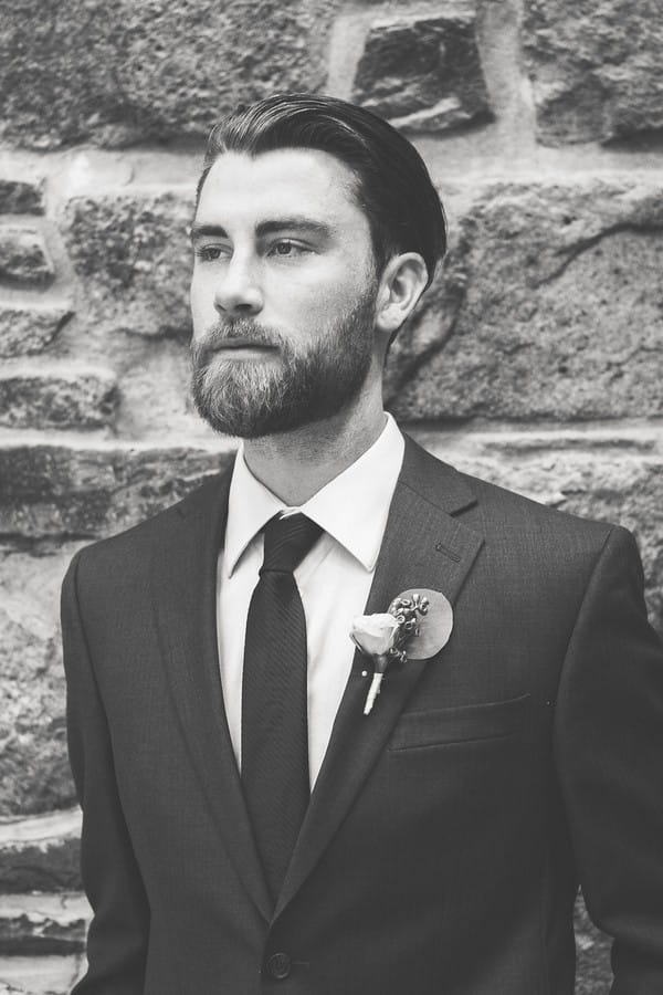 Groom standing up against brick wall