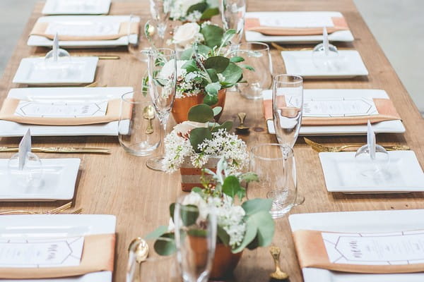 Copper pots of flowers down centre of wooden wedding table