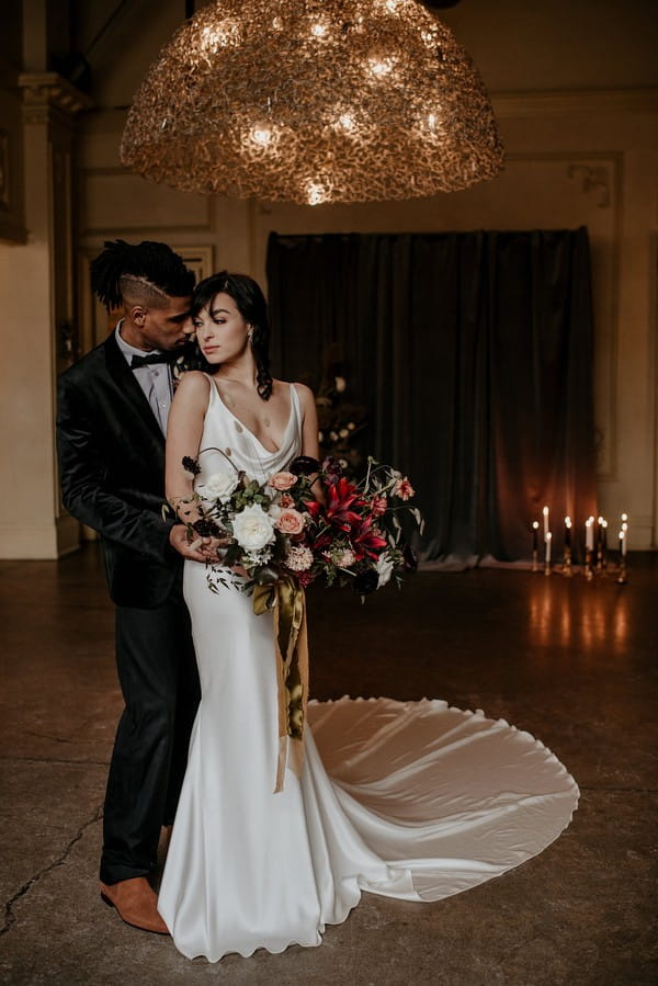 Groom standing behind bride holding large autumnal bouquet