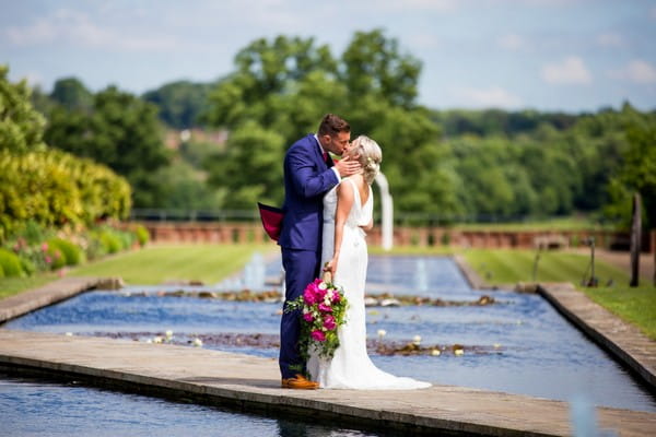 Bride and groom kissing on bridge over venue water feature - Picture by Joss Denham Photography