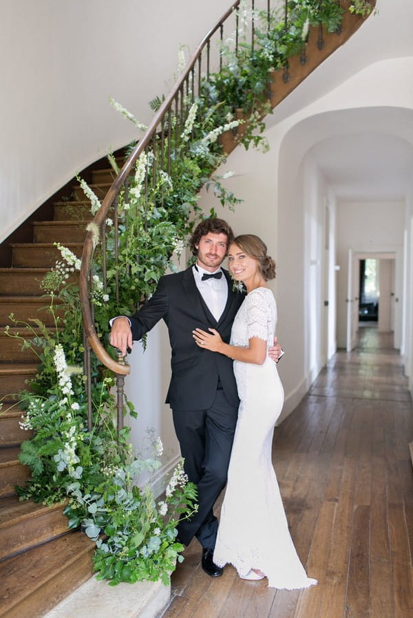 Bride and groom standing by staircase of Chateau de Redon covered in foliage