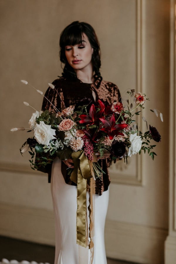 Bride in velvet shrug holding autumnal bouquet