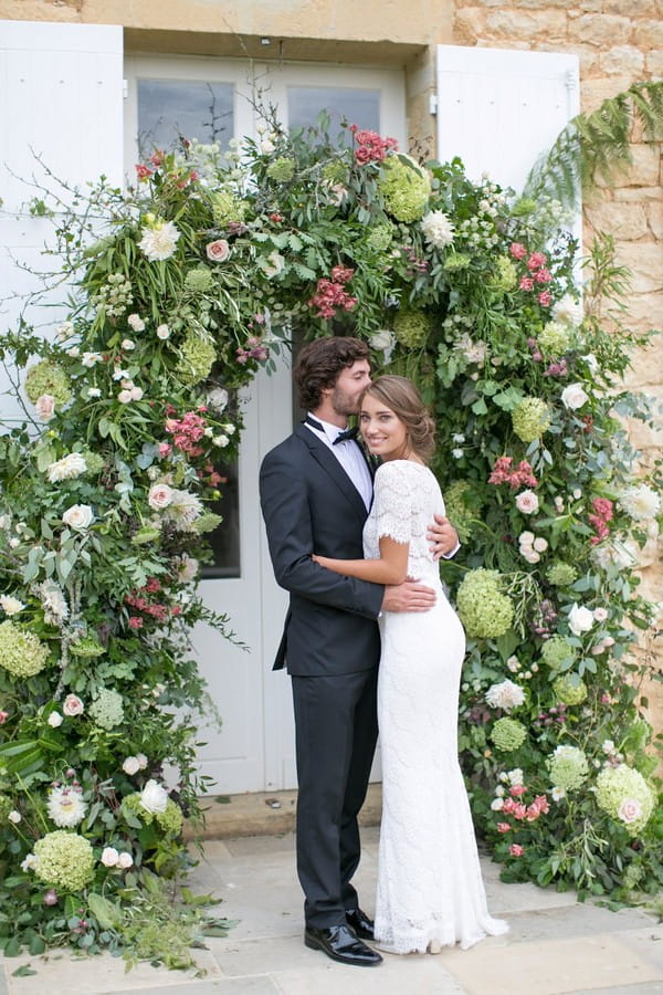 Bride and groom in front of flower and foliage arch