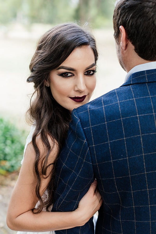 Bride with dark make-up looking over groom's shoulder