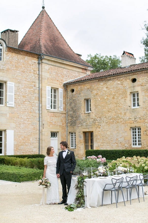 Bride and groom standing by wedding table outside Chateau de Redon