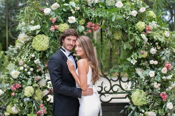 Bride and groom in front of large flower and foliage arch
