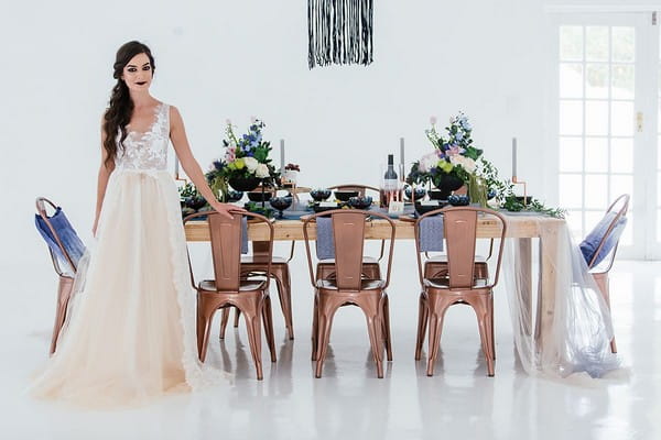 Bride standing in front of wedding table with blue and copper styling