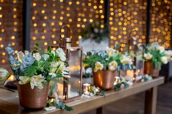 Copper pots of flowers and lanterns on wedding table