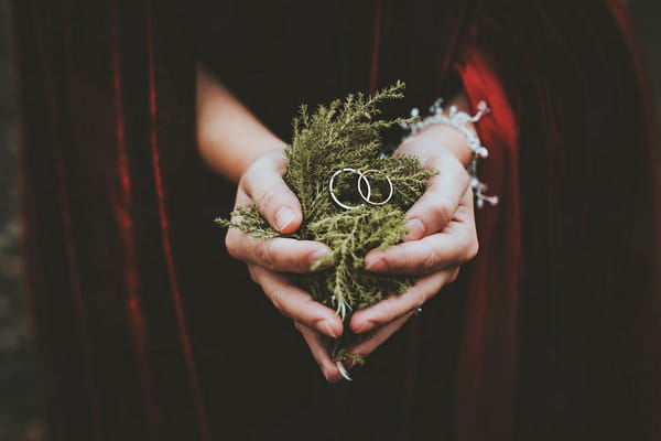 Bride holding handful of fern with wedding rings on top