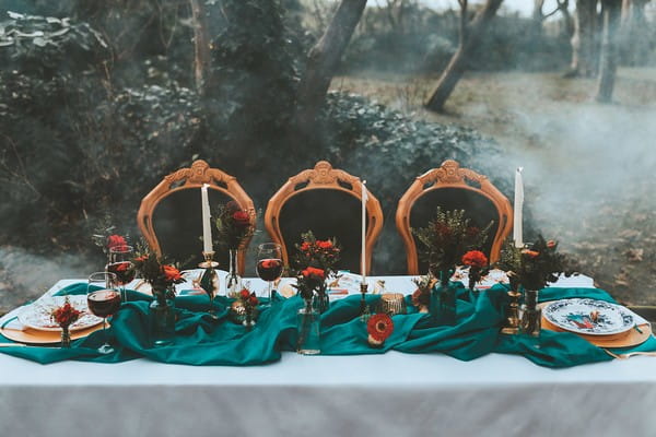 Wedding table in woods with teal runner and red flowers