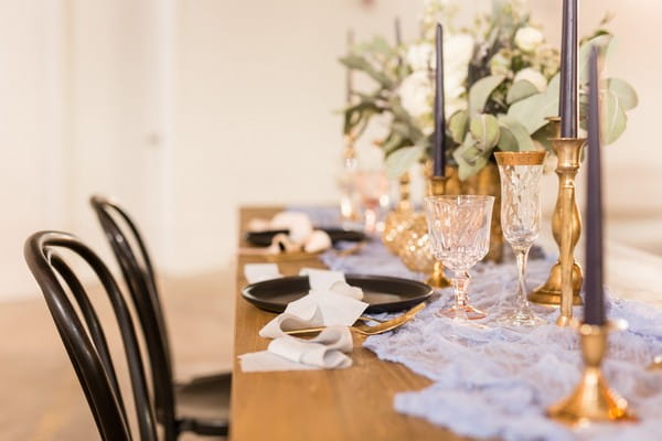 Elegant wedding table styling with black plates, tulle table runner and gold candlesticks