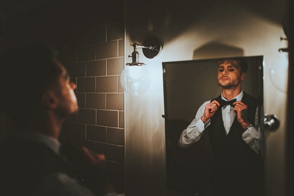 Groom doing up bow tie in mirror