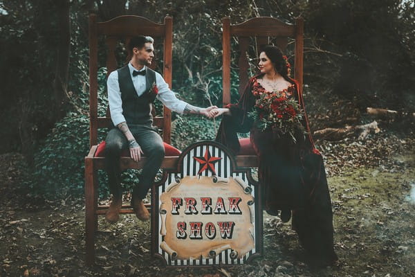 Bride and groom sitting on chairs next to 1920's carnival freak show sign