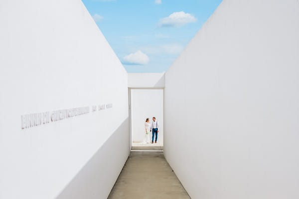 Bride and groom standing at end of long passageway with blue sky overhead - Picture by David Deman