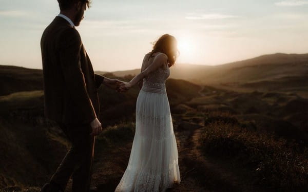 Bride leading groom by the hand as they walk across hills - Picture by The Kitcheners