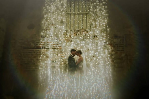 Bride and groom standing in front of fairy light backdrop - Picture by Jamie Sia Photography