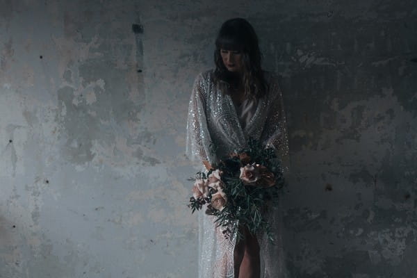 Bride holding bouquet standing against warehouse wall