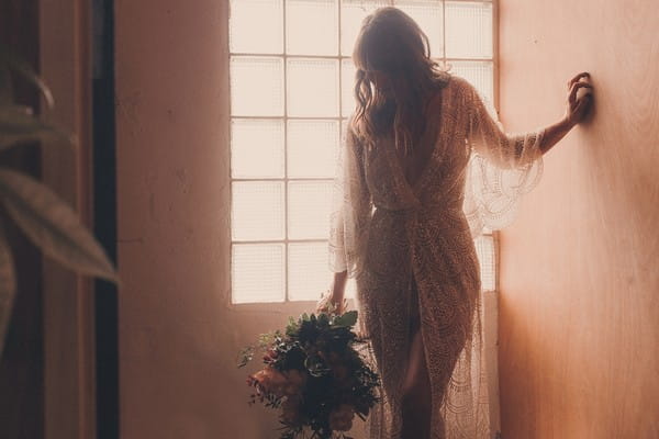 Bride holding bouquet in front of window