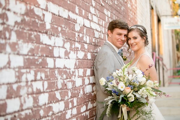 Bride and groom touching heads leaning against wall