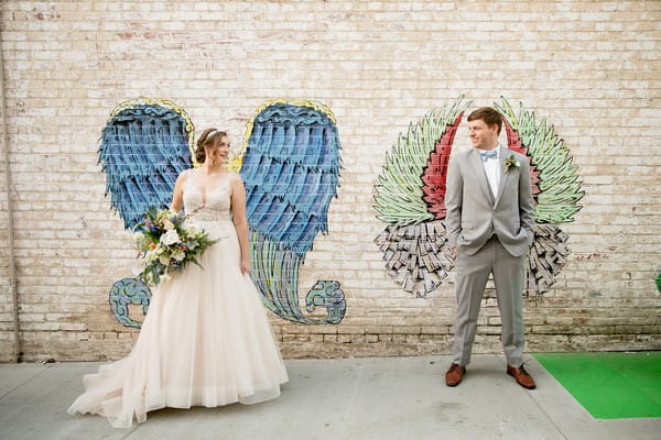 Bride and groom standing in front of wing graffiti artwork on wall