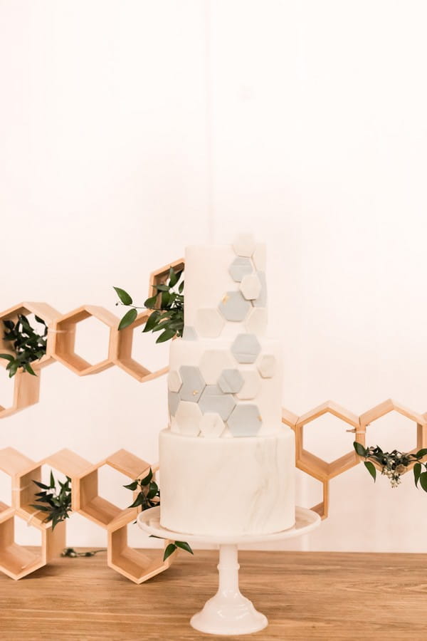 Wedding cake with hexagon detail in front of honeycomb shaped backdrop