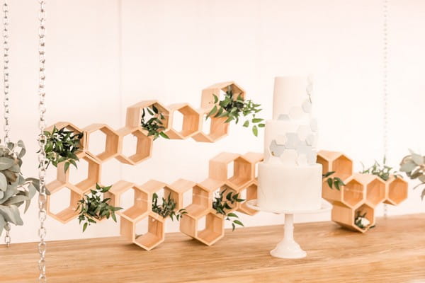 Wedding cake with hexagon detail in front of honeycomb style backdrop