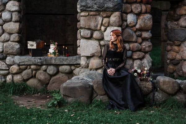 Gothic bride sitting on rocks by castle