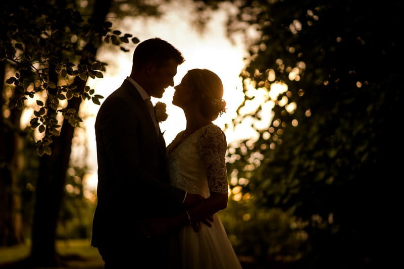 Bride and groom facing each other as light shines through trees behind them