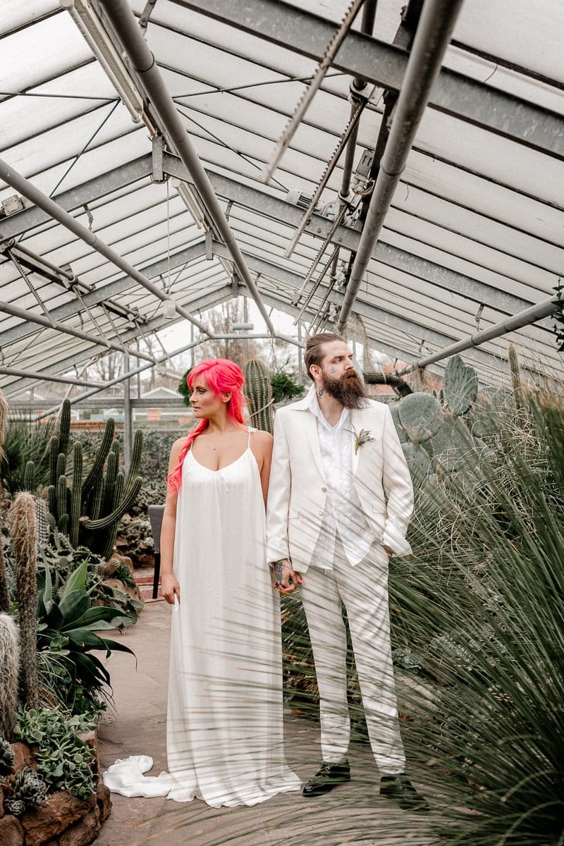 Bride with pink hair holding hands with groom in white suit