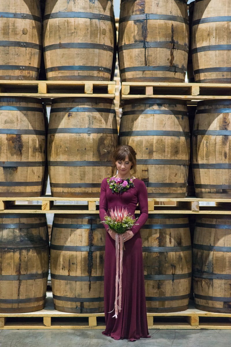 Bridesmaid in purple dress standing in front of barrels at Breckenridge Distillery