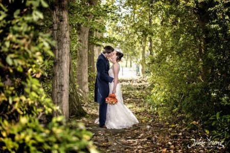 Bride and groom kissing by trees in woodland - Picture by John Young Photography