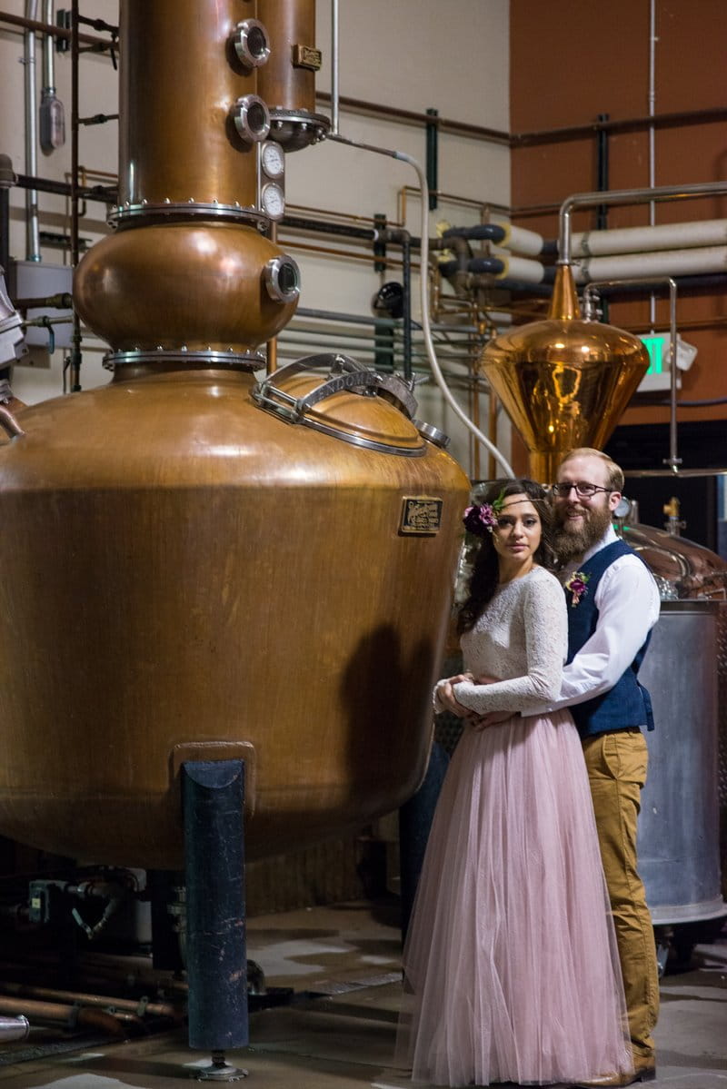 Bride and groom in front of distillery equipment