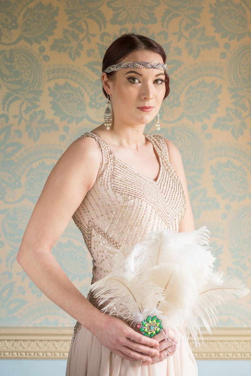 Bridesmaid wearing mink dress and vintage style headband holding feathers