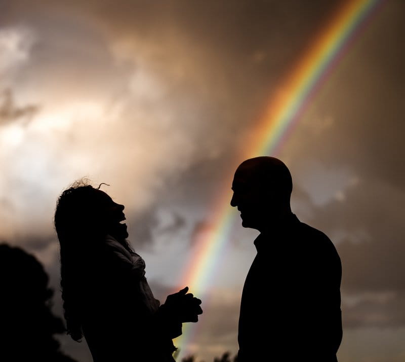 Silhouette of wedding guests talking with rainbow in background