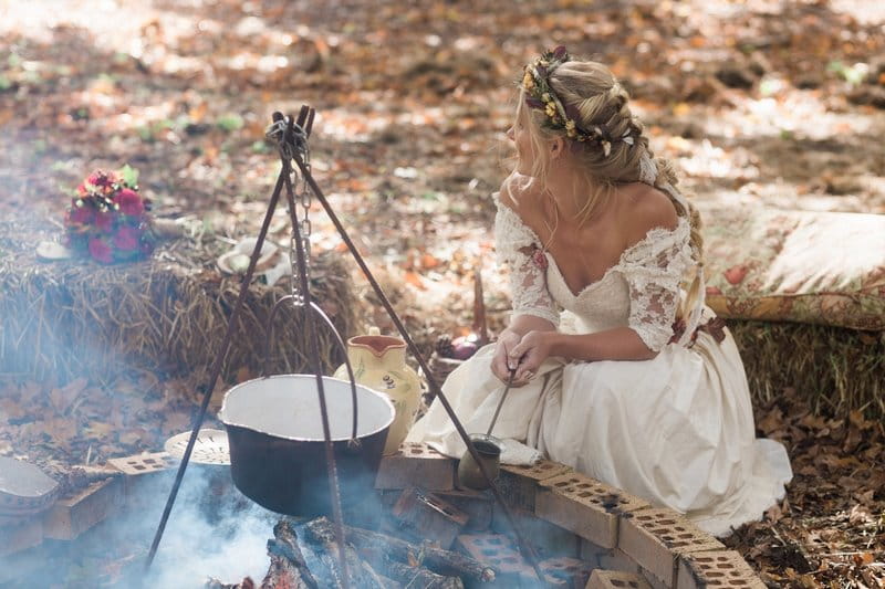 Bride crouching by open fire in woodland