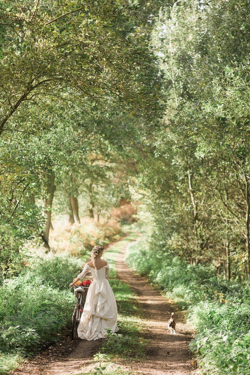 Bride walking through woodland with bicycle