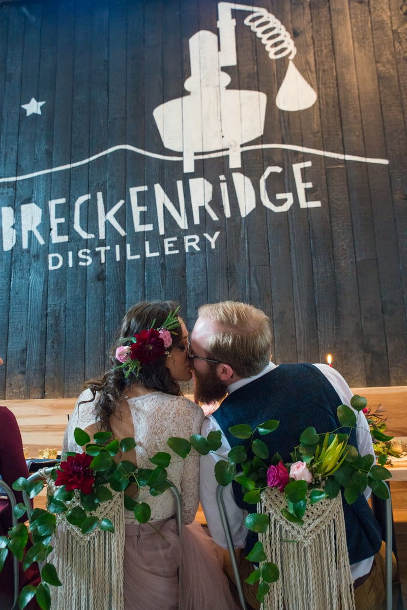 Bride and groom kissing in front of Breckenridge Distillery sign