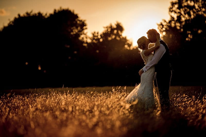 Bride and groom kissing in field as sun sets