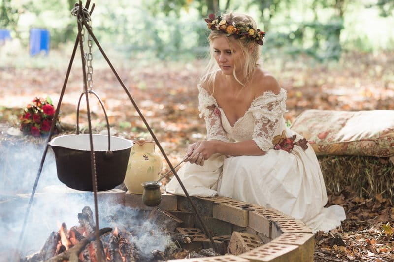 Bride holding pot over open fire in woodland