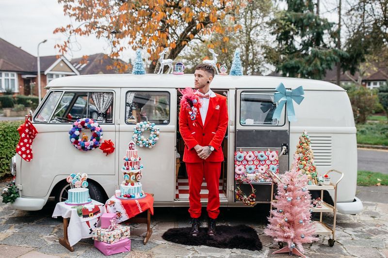 Groom in red suit standing outside VW Camper Van surrounded by Christmas kitsch items