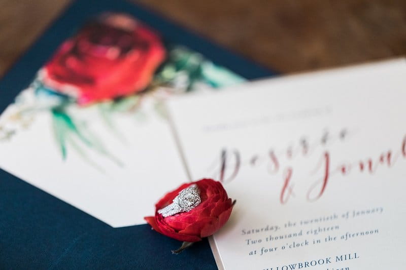 Wedding ring on red flower on top of wedding stationery