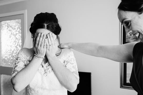 Bridesmaid smiling with hand on bride's shoulder ans bride covers face with her hands - Picture by Ally Stuart Photography