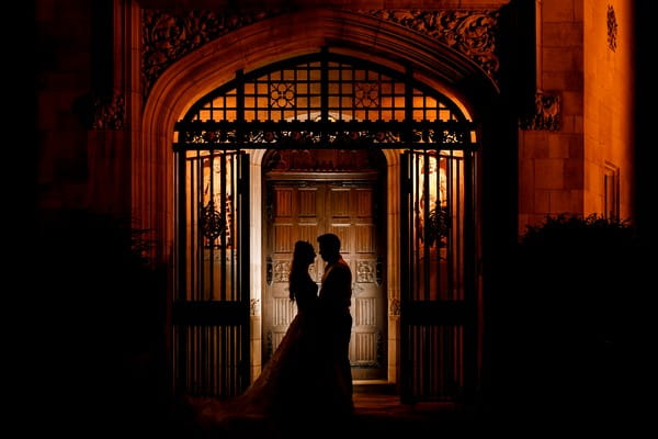 Bride and groom standing at gated good of wedding venue at night - Picture by Damion Mower Photography