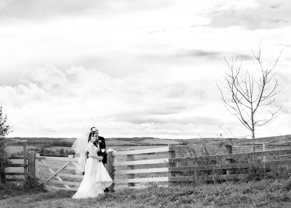 Bride and groom standing by gate to field in countryside - Picture by Rosie Cutbill Photography