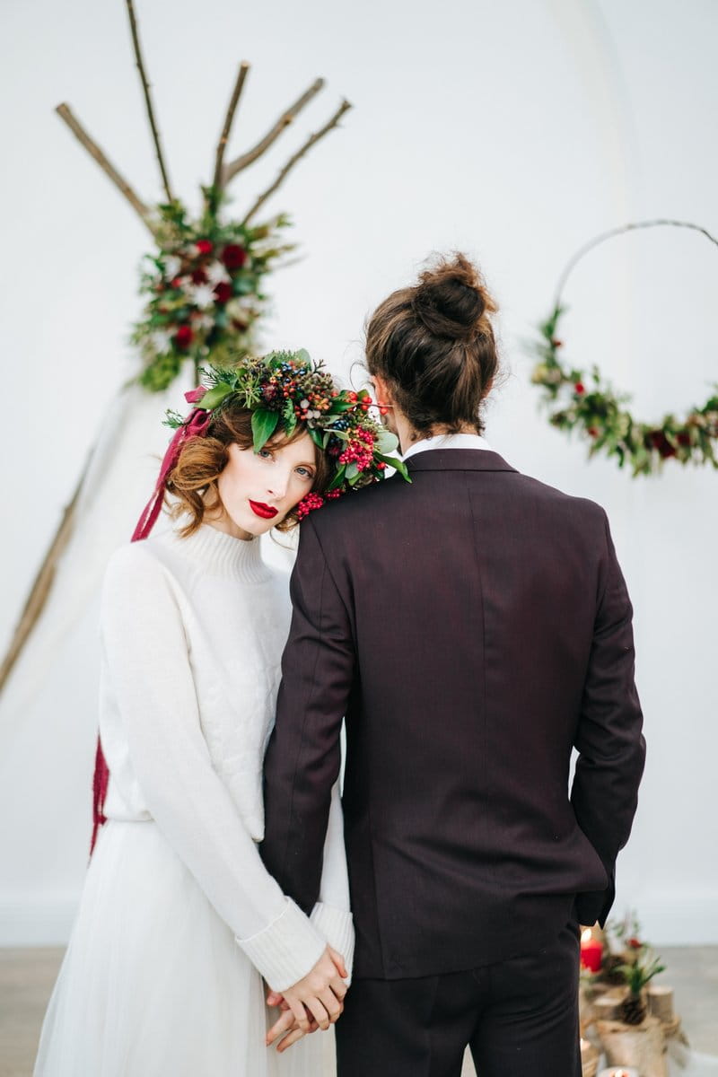 Bride with red berry and foliage crown holding groom's hand